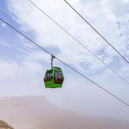Tolip Resort El Galala Majestic Ain Sukhna Extérieur photo The photo shows a green cable car suspended in the air, traveling along overhead cables. The backdrop features a hazy landscape, likely mountainous or elevated terrain, with a cloudy sky. The scene suggests a scenic transportation method, possibly us