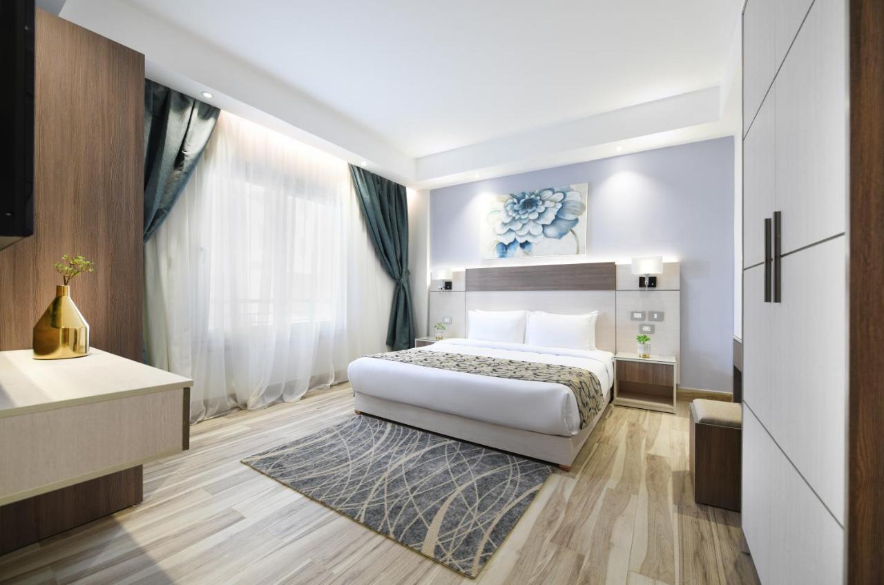 Tolip Resort El Galala Majestic Ain Sukhna Extérieur photo The photo shows a modern bedroom with a clean and stylish design. It features a large bed with white bedding positioned against a wall. Above the bed, there is a decorative artwork, possibly a floral design. The room has large windows with sheer curt