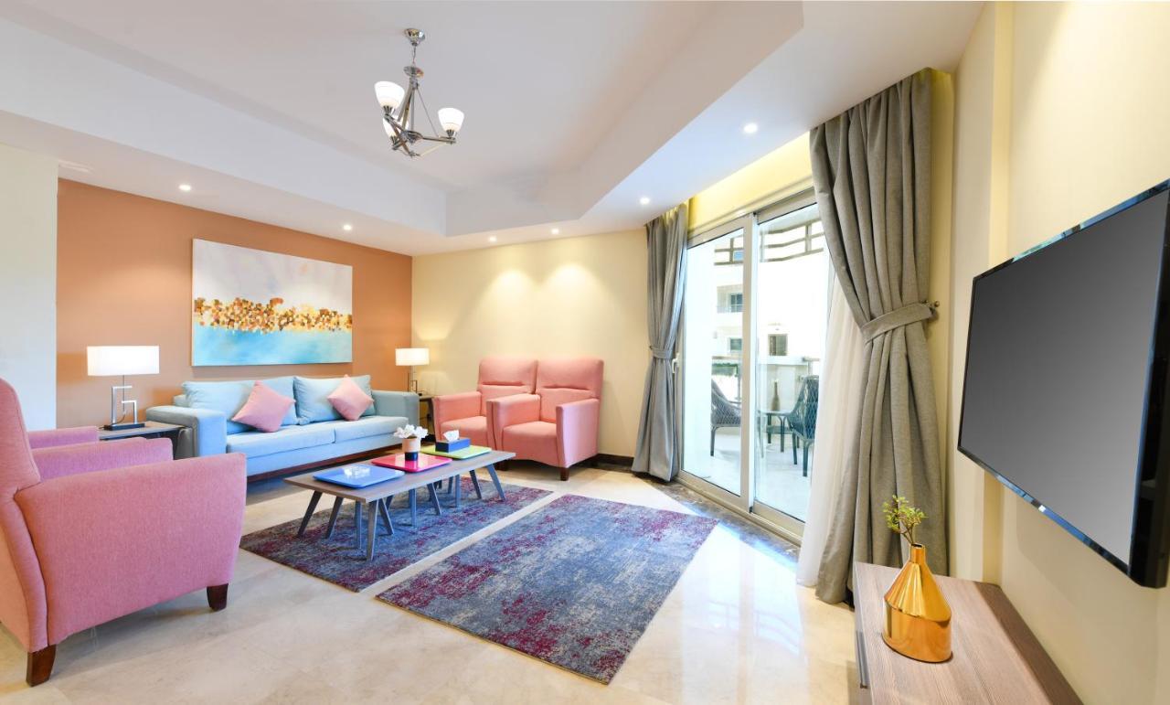 Tolip Resort El Galala Majestic Ain Sukhna Chambre photo The photo shows a modern living room that features a cozy and stylish design. There is a light blue sofa adorned with pastel pink cushions, accompanied by two pink armchairs. A coffee table sits in front, placed on a colorful area rug that adds warmt