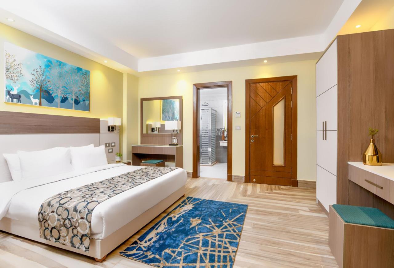 Tolip Resort El Galala Majestic Ain Sukhna Extérieur photo The photo shows a well-decorated hotel room. There is a large bed with white linens and a decorative throw blanket. The room features a wooden wardrobe and a bedside table with lamps. A colorful rug is placed on the floor, adding warmth to the space.