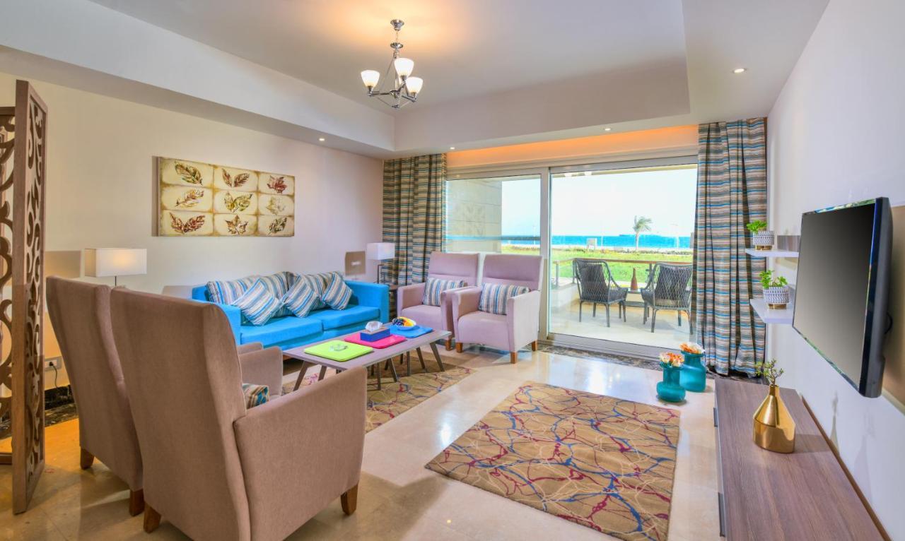 Tolip Resort El Galala Majestic Ain Sukhna Extérieur photo The photo shows a bright and modern living room. It features a blue sofa with decorative cushions, two light-colored armchairs, and a coffee table. A large area rug adds warmth to the space, which is decorated with a subtle pattern. The walls have so