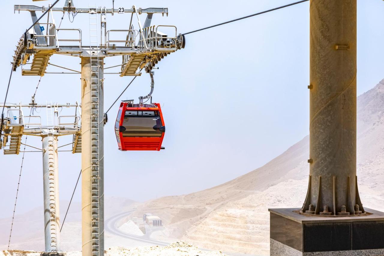 Tolip Resort El Galala Majestic Ain Sukhna Extérieur photo The photo shows a cable car system with a single red gondola suspended mid-air. It appears to be part of a larger cable car infrastructure, with metal pylons supporting the cables above. The background features a hazy landscape, likely characterized 