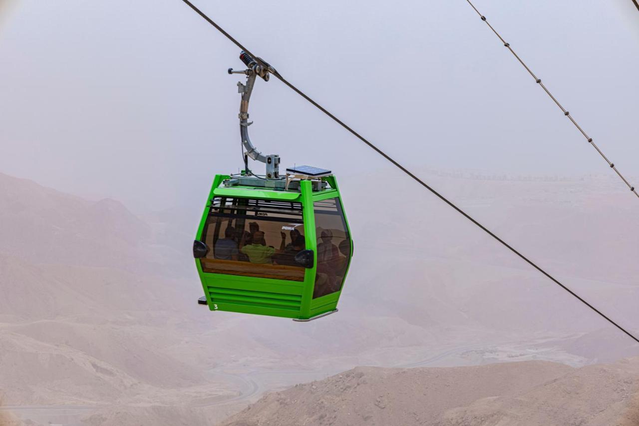 Tolip Resort El Galala Majestic Ain Sukhna Extérieur photo The photo shows a green cable car suspended in the air, moving along a wire. The cable car appears to be traversing a mountainous landscape, which looks rocky and arid. The surrounding environment is somewhat foggy or hazy, suggesting limited visibil