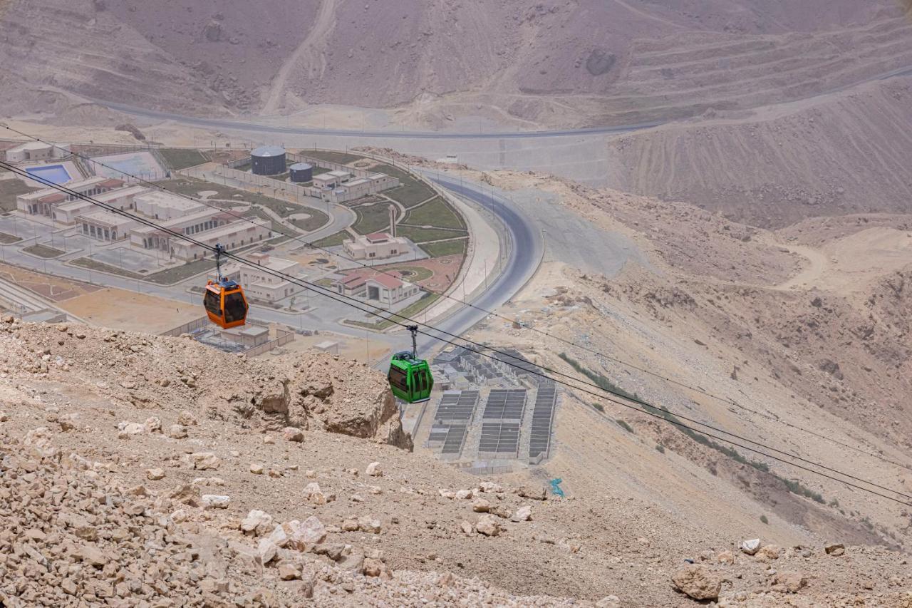 Tolip Resort El Galala Majestic Ain Sukhna Extérieur photo The photo shows a scenic view from a high elevation, featuring a cable car system. Two cable cars are visible, one orange and one green, traveling along cables down the mountainside. Below, there appears to be a developed area with roads and light st