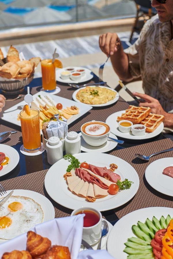 Tolip Resort El Galala Majestic Ain Sukhna Extérieur photo The photo shows a breakfast spread laid out on a table. There are several plates with a variety of food items, including:

1. **Sliced Cold Cuts**: A plate featuring various cold meats, accompanied by garnishes like cherry tomatoes and lettuce.
2. **