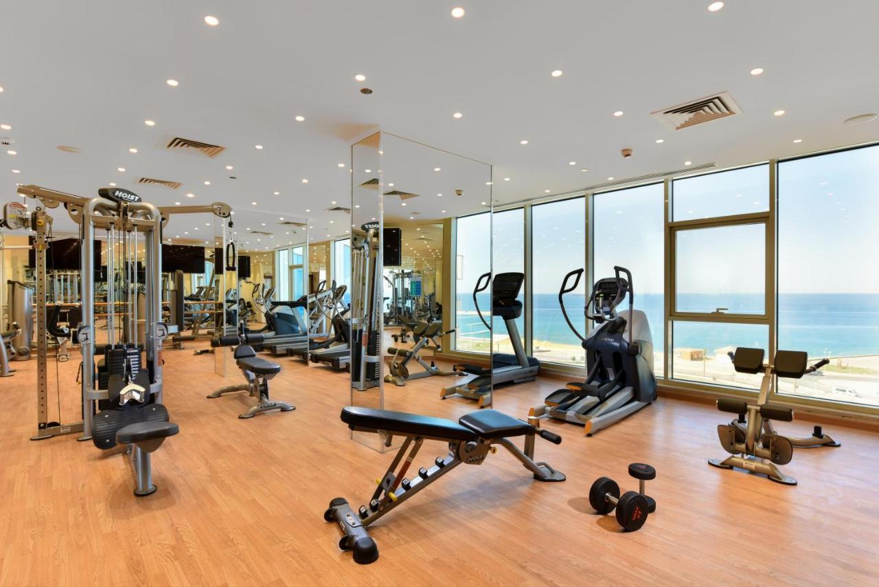 Tolip Resort El Galala Majestic Ain Sukhna Extérieur photo The photo shows a modern gym interior with a variety of fitness equipment. There are cardio machines like treadmills and ellipticals, along with strength training equipment such as free weights and benches. The gym features large windows that offer a