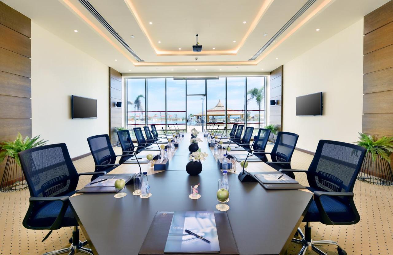 Tolip Resort El Galala Majestic Ain Sukhna Extérieur photo The image shows a modern conference room with a large, dark rectangular table surrounded by ergonomic black chairs. The room features large windows that allow natural light to enter and provide a view of the outdoors, including some greenery. On the 