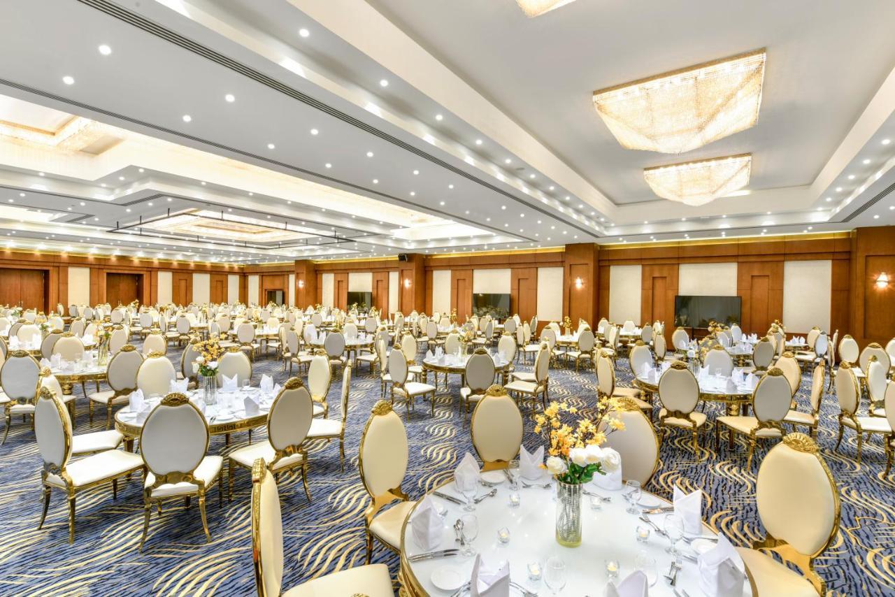 Tolip Resort El Galala Majestic Ain Sukhna Extérieur photo The photo shows a spacious and elegantly decorated banquet hall. The room features numerous round dining tables, each set with white tablecloths and adorned with decorative centerpieces, likely flowers. The chairs surrounding the tables have a luxuri
